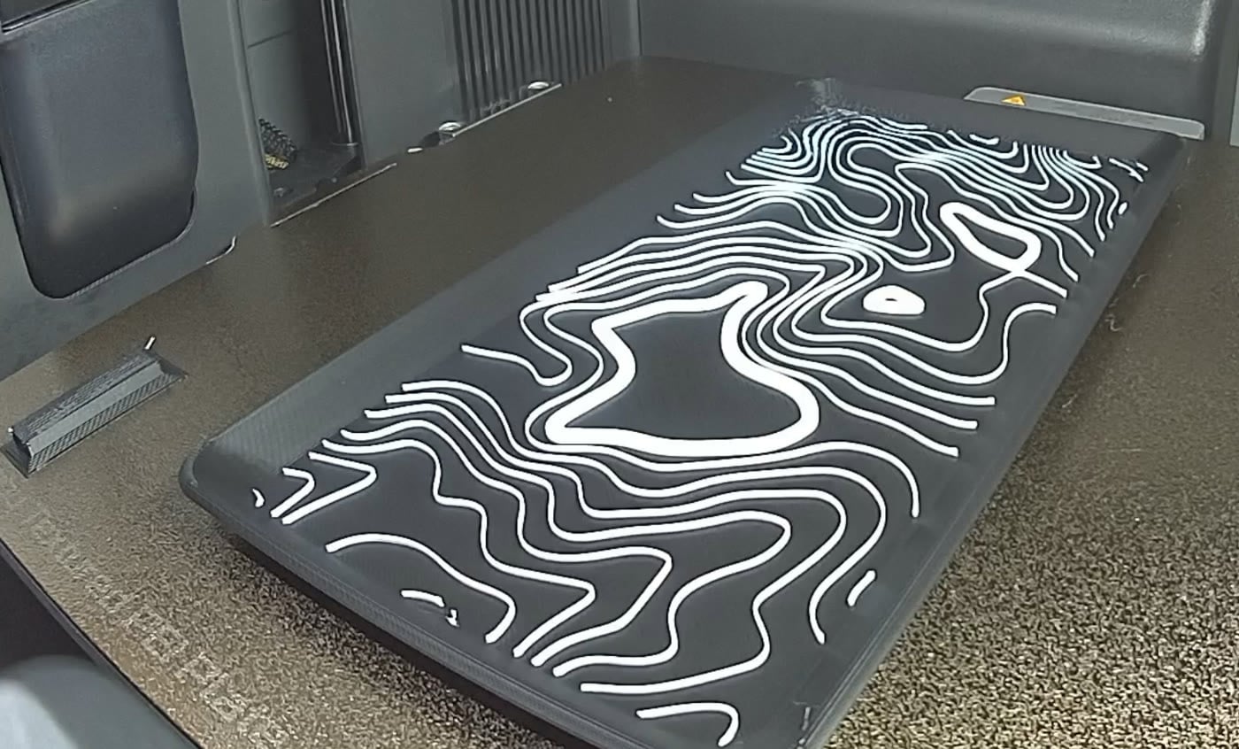A black 3D-printed tray with a raised white contour-map pattern