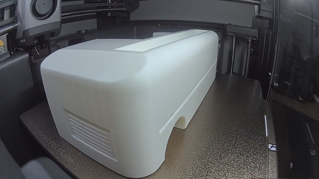 A large white 3D-printed equipment housing with a vent grille on the print bed
