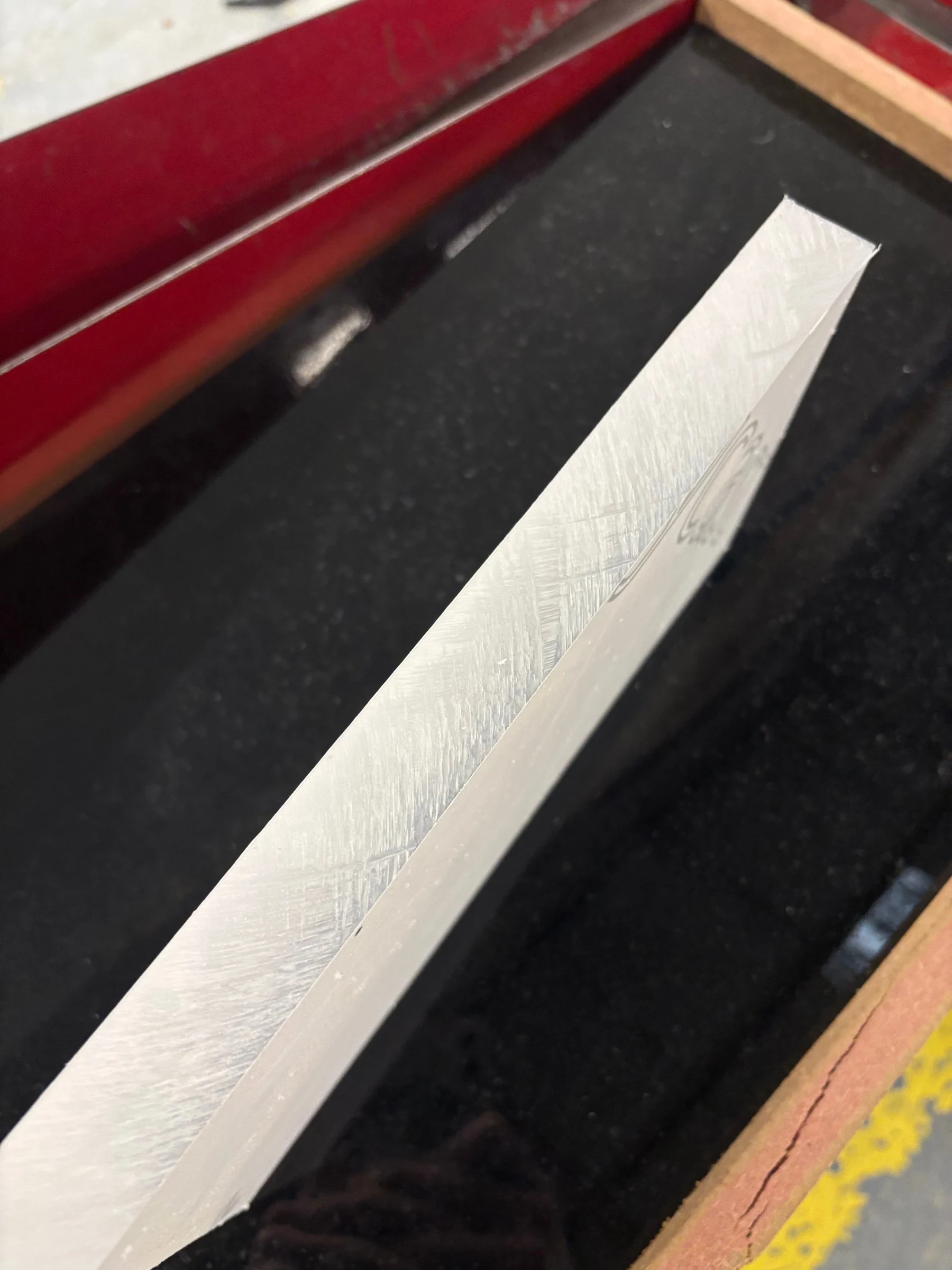 The edge of a clear acrylic sheet on the polisher's black bench, close up