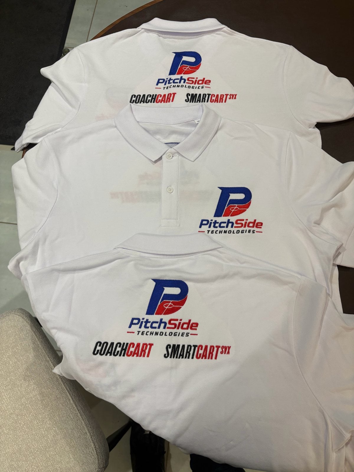 Three white polo shirts embroidered with the PitchSide Technologies logo, front and back