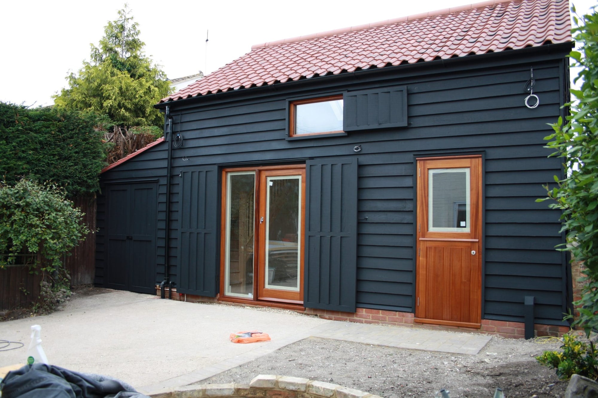 A completed barn conversion in black timber cladding with hardwood doors and a clay tiled roof