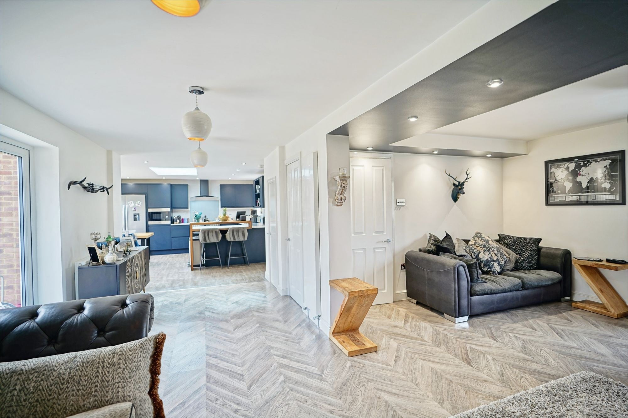 An open-plan living space looking through to the kitchen, herringbone floor and a dropped ceiling detail